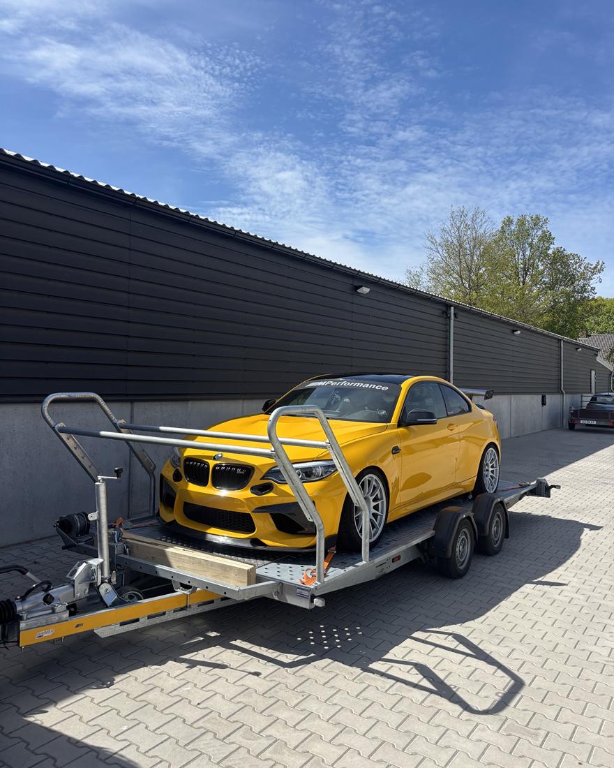 Gele BMW M2 met M Performance-striping, vastgezet op de aanhanger